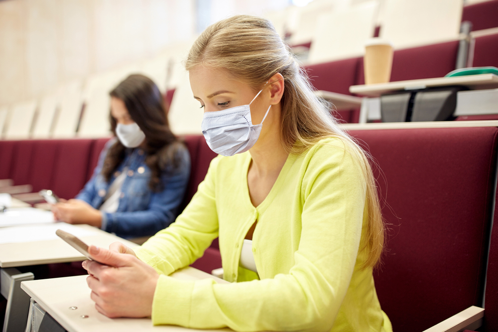 student girls wearing face protective medical masks for protection from virus disease with smartphones on lecture
